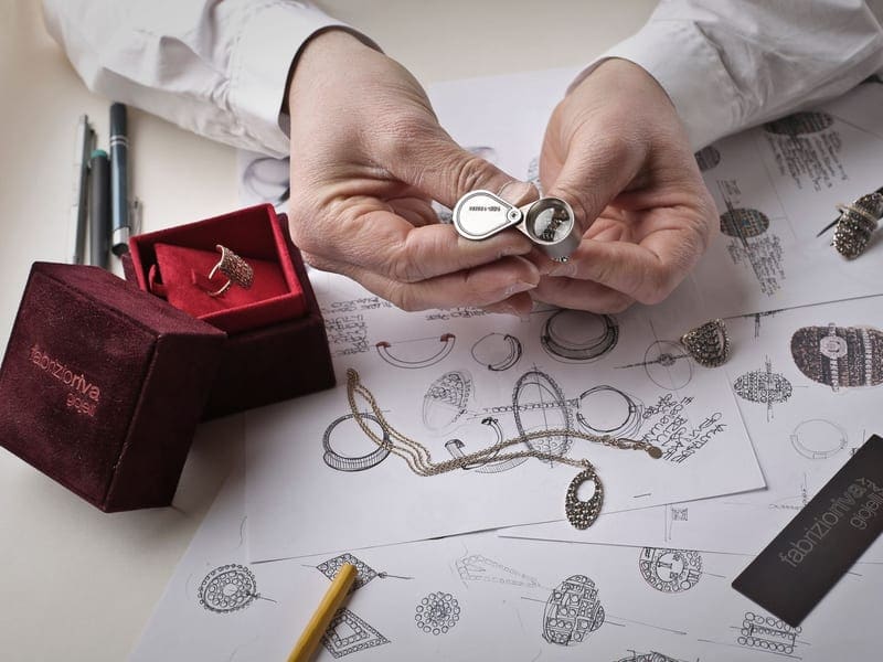 Designer inspecting a ring with a loupe over jewelry sketches