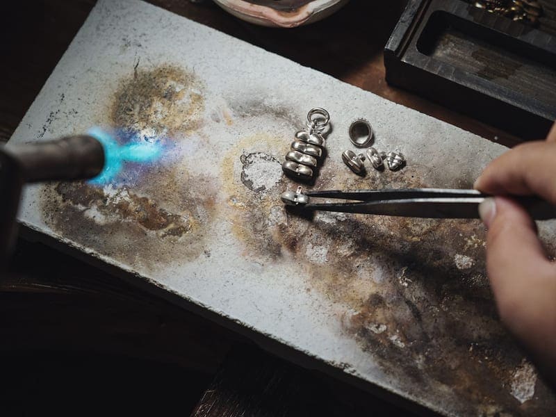 Jeweler using a torch to solder metal on a workbench