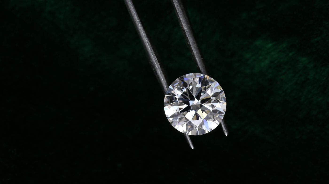 Loose round diamond held in tweezers under studio light