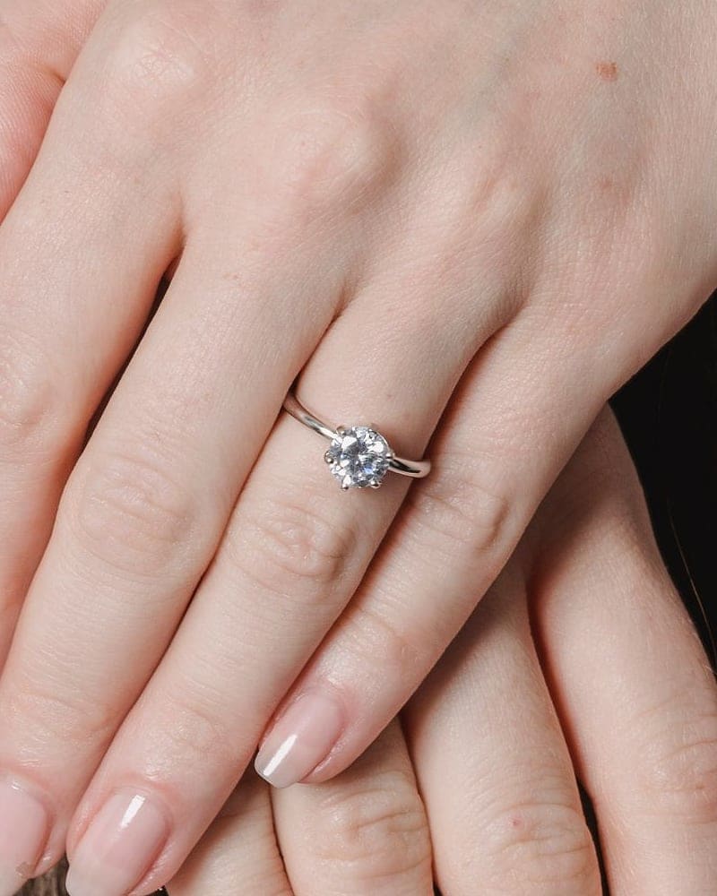 Hands resting on dark hair, wearing a delicate diamond solitaire ring