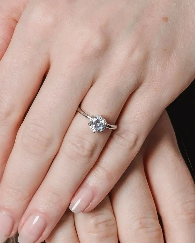 Hands resting on dark hair, wearing a delicate diamond solitaire ring