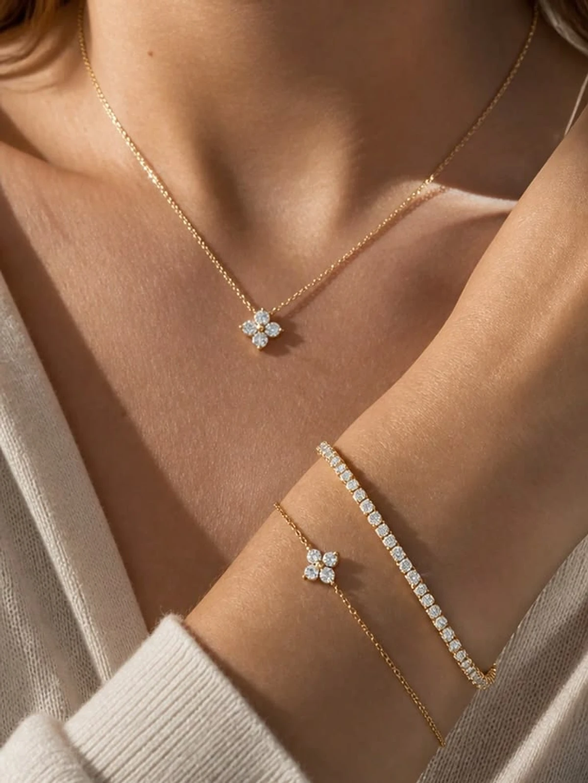 Gold clover bracelet layered with a diamond tennis bracelet and a cream knit sleeve