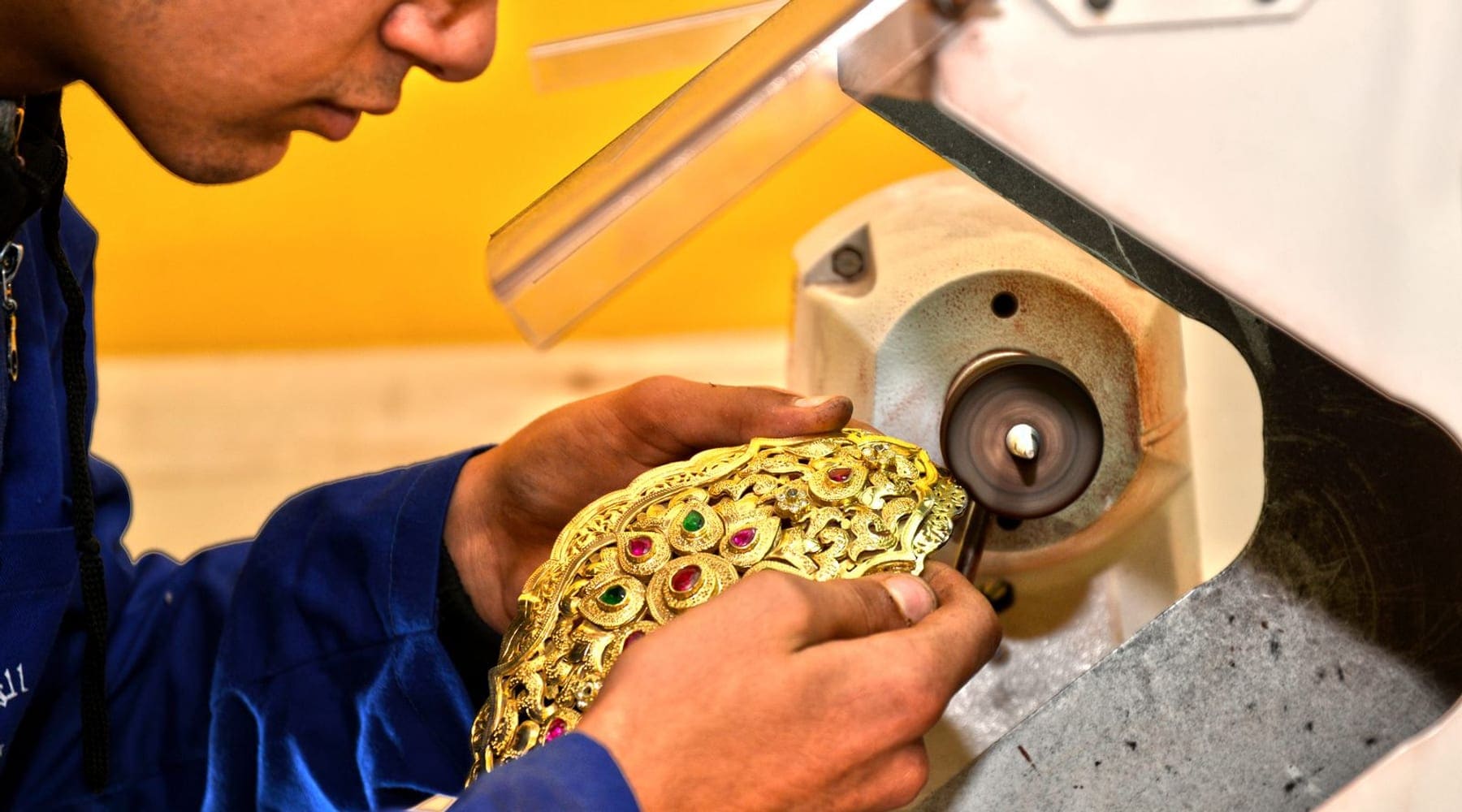 Artisan polishing an ornate gold piece on a workshop wheel