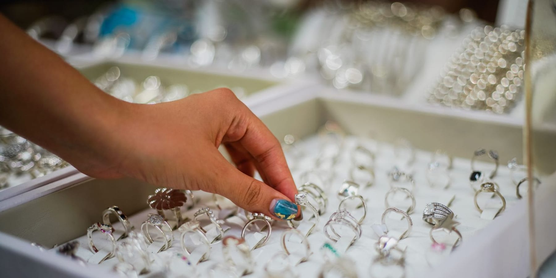 Hand choosing a diamond ring from a tray of rings in a showcase